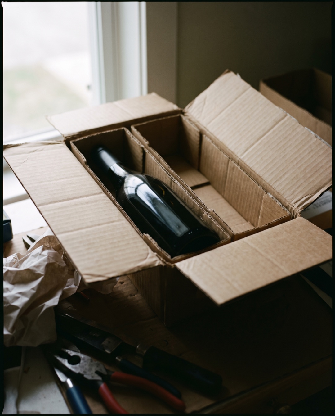 A single wine bottle sits in one compartment of a two-bottle cardboard shipping insert; the second compartment is empty.