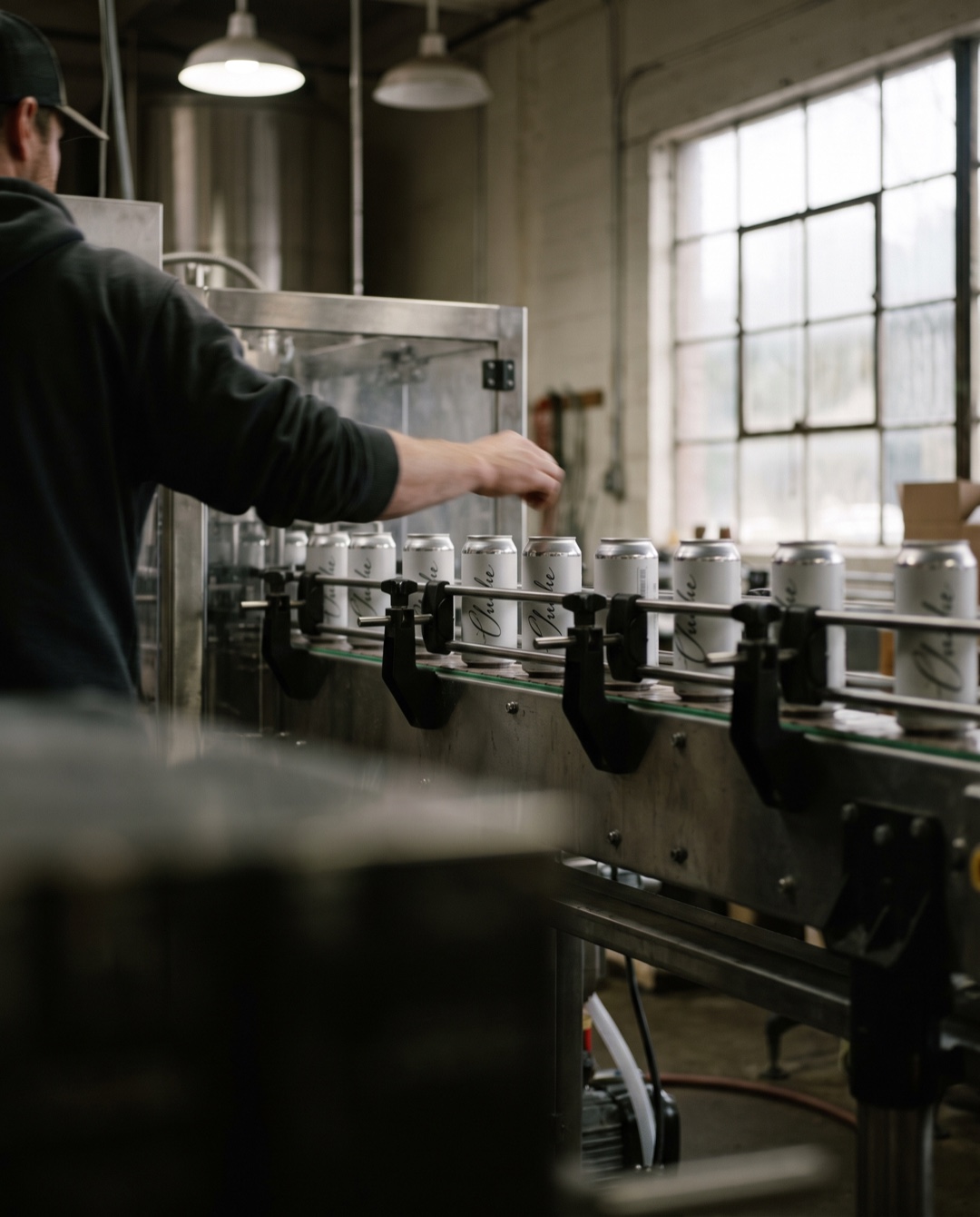 Slim wine cans stream along a canning line conveyor, each printed with a small cursive flourish.