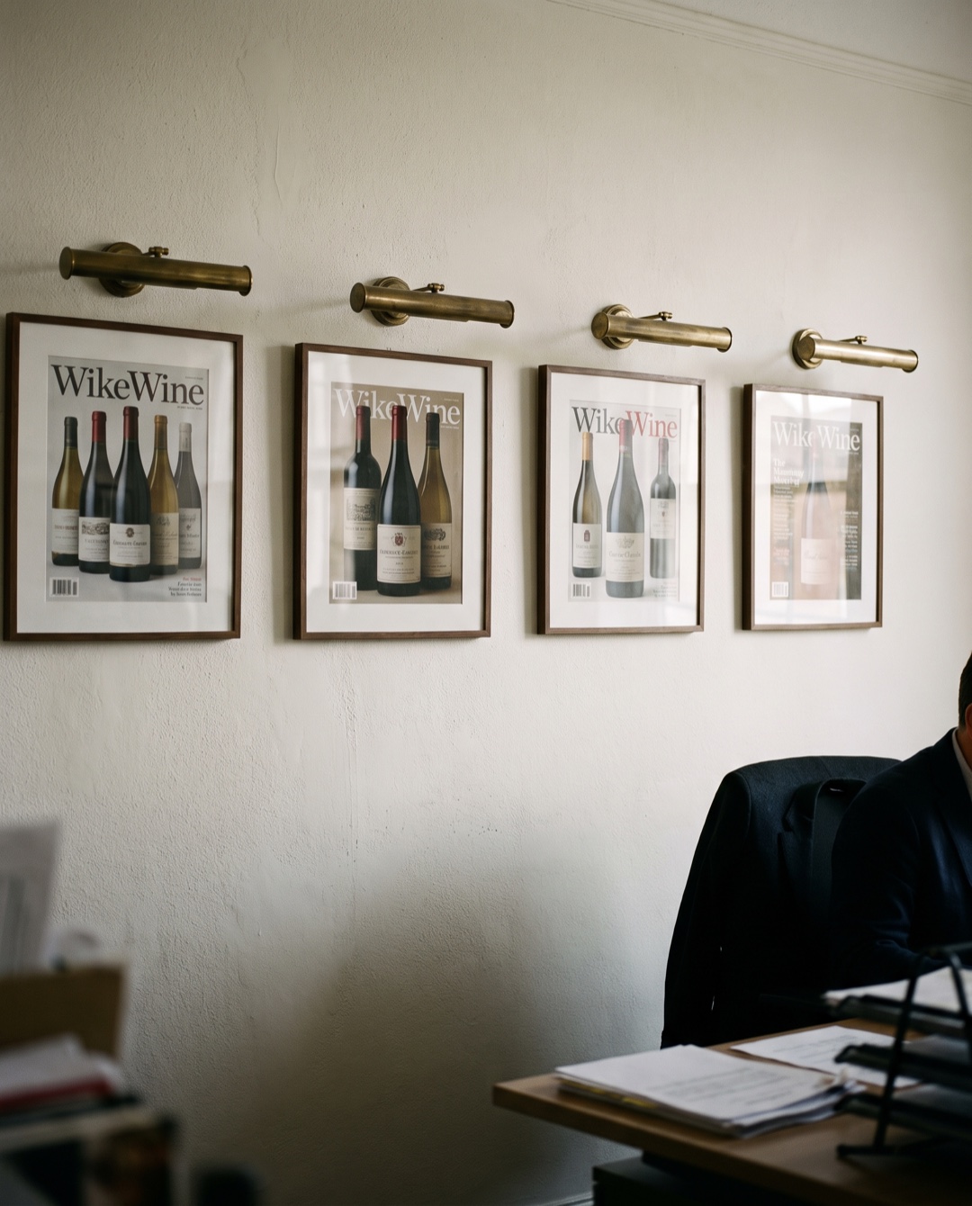 Four framed magazine covers hang in a row on an office wall, each featuring a wine bottle photograph.